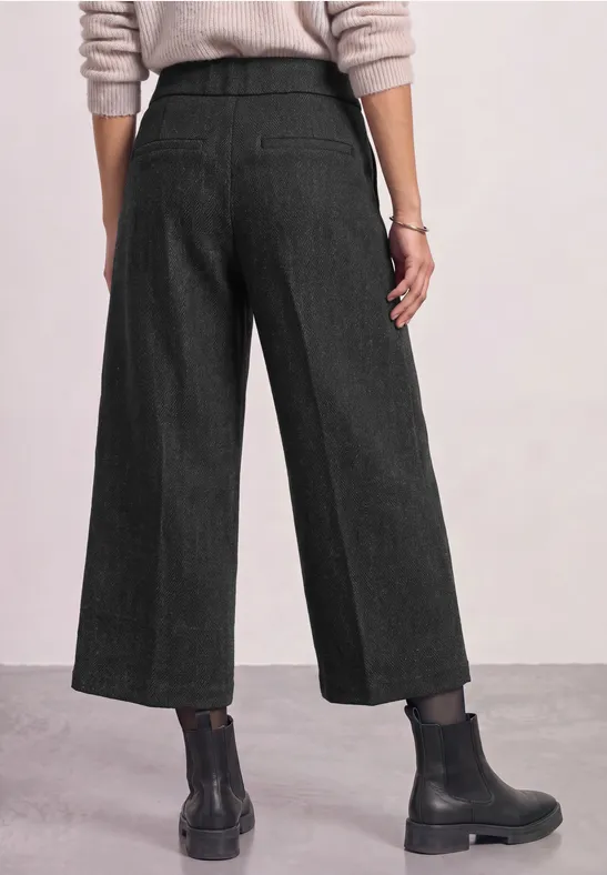 Vue de dos : pantalon large noir aux chevilles, pull clair et bottines noires.