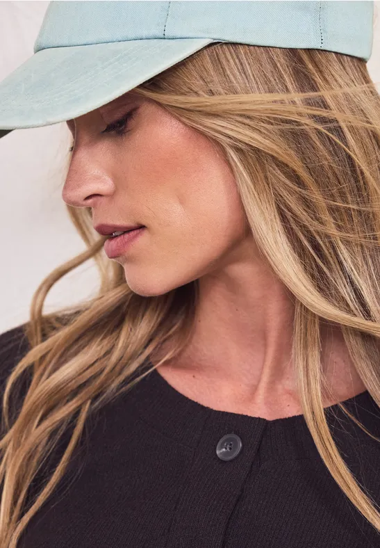 Personne aux longs cheveux blonds, casquette bleu clair et vêtement sombre, visage flou.