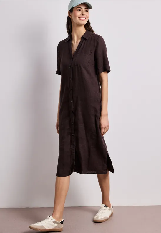 Femme en robe-chemise midi marron foncé, manches courtes, fentes latérales, baskets beiges et casquette.