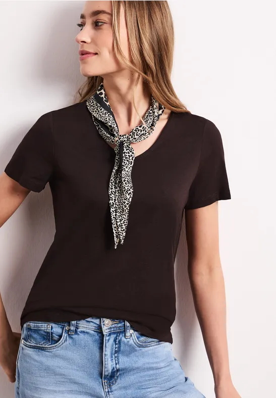 Kobieta w czarnym t-shicie, jasnoniebieskich jeansach i wzorzystej apaszce, twarz rozmyta.