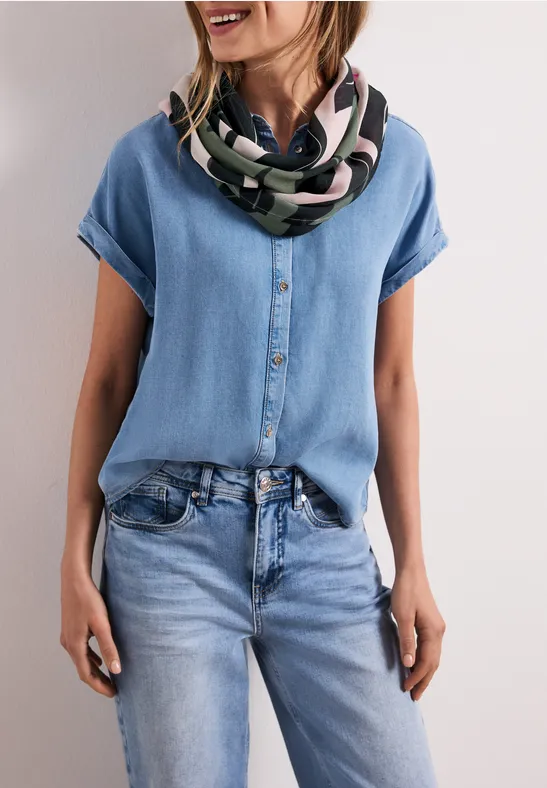 Kobieta ma na sobie jasną dżinsową bluzkę i jeansy oraz kolorowy szal.