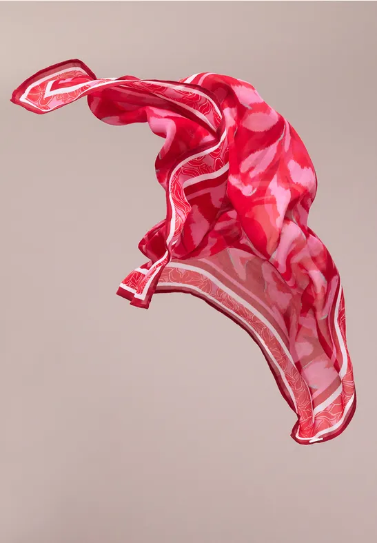 Czerwona apaszka w wzory unosi się lekko w powietrzu na neutralnym tle.