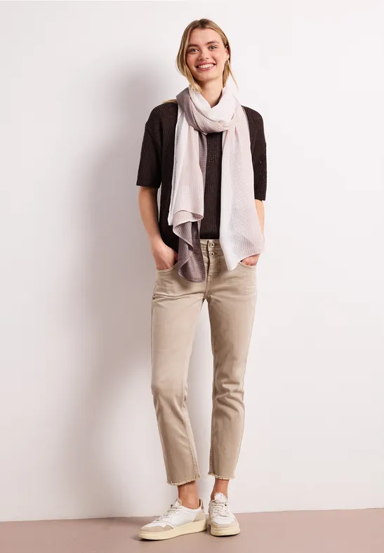 Osoba ma na sobie beżowe chinosy, białe trampki, czarny t-shirt i jasny szalik.