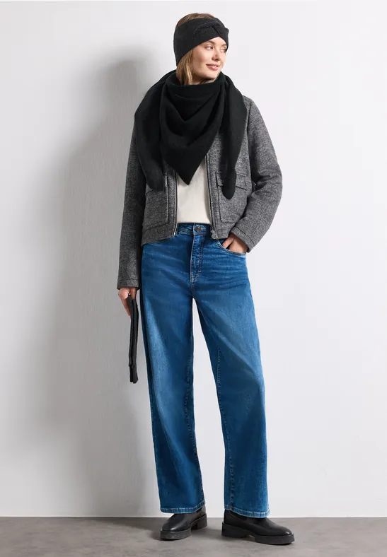 Frau in schwarzer Mütze und Schal, grauer Jacke, beigem Shirt, weiten Jeans und schwarzen Schuhen.