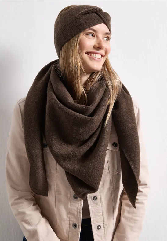 Lächelnde Frau im braunen Dreieckstuch und Stirnband, trägt eine beige Jacke.