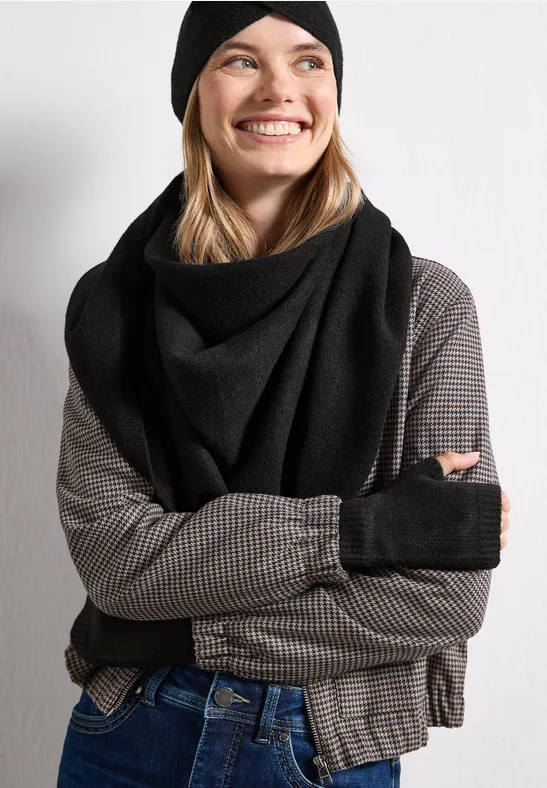 Lächelnde Frau mit schwarzer Mütze, Schal, fingerlosen Handschuhen, kariertem Shirt und Jeans.