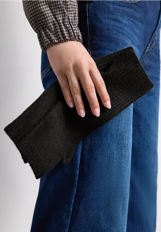 Person in Jeans und Hemd hält einen schwarzen Strickschal in der Hand.