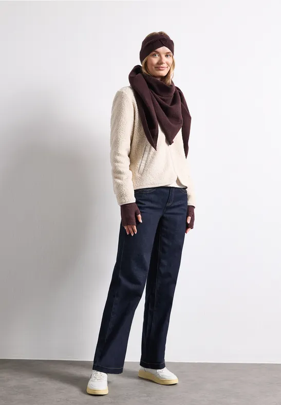 Frau in stylischer Wintermode: heller Pullover, dunkelrote Mütze und Tuch, Handschuhe, dunkle Jeans und weiße Sneaker.