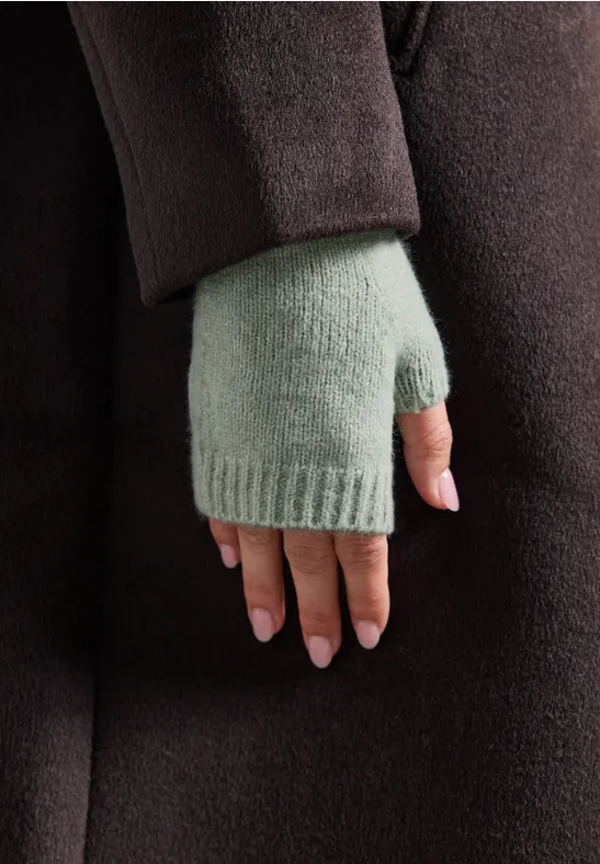 Nahaufnahme einer Hand in hellgrünem Fingerhandschuh und dunkelbraunem Mantel.
