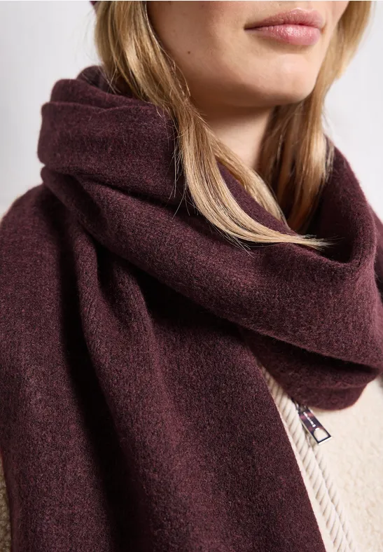 Une écharpe bordeaux en laine, drapée autour du cou, portée avec un pull crème.