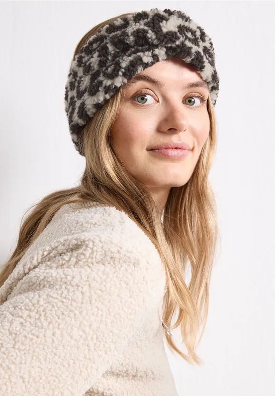Eine junge Frau mit hellem Teint trägt ein flauschiges Stirnband und eine Teddyjacke, seitlicher Blick zur Kamera.