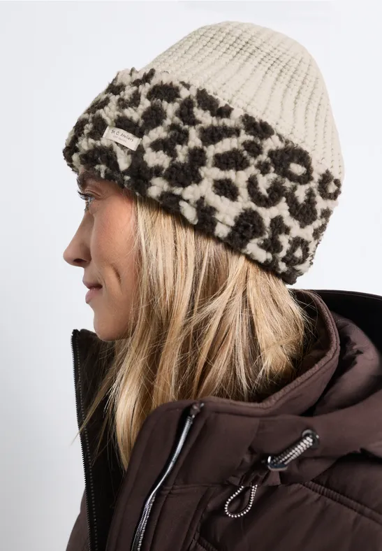 Seitenansicht einer Frau mit beiger Strickmütze mit Leopardenmuster und brauner Winterjacke.