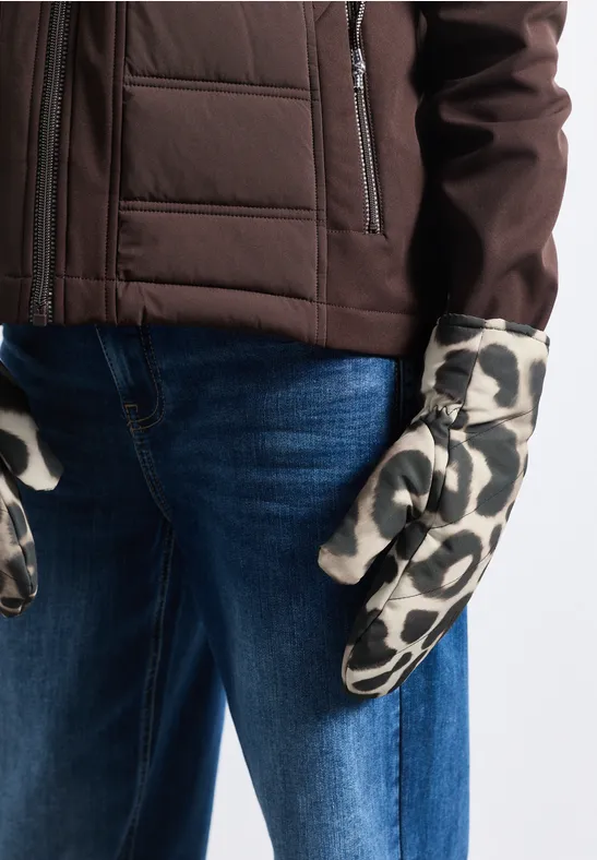 Person trägt braune Jacke, blaue Jeans und weiße Handschuhe mit schwarzen Fleckenmuster.