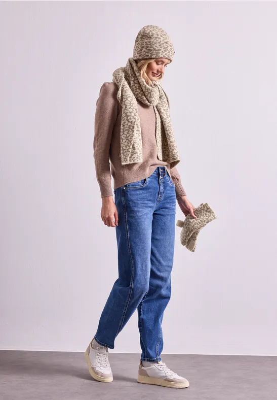 Frau in Jeans, rosa Pullover, Strickmütze, Schal und Handschuhe hält einen Handschuh