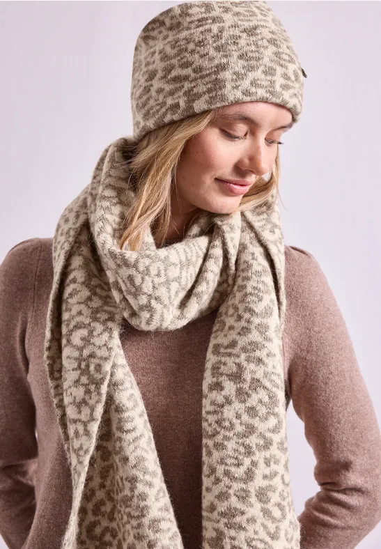 Frau trägt beige-braunen Strickhut und passenden Schal mit Leopardenmuster, dazu brauner Pullover