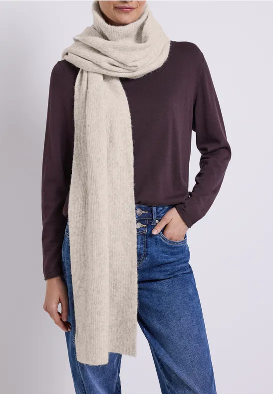 Person trägt fliederfarbene Langarmbluse, blaue Jeans und langen cremefarbenen Schal um den Hals.