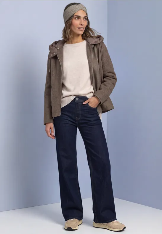 Frau in Freizeitlook mit beigem Pullover, khakifarbener Jacke, weiten Jeans und beigen Schuhen.