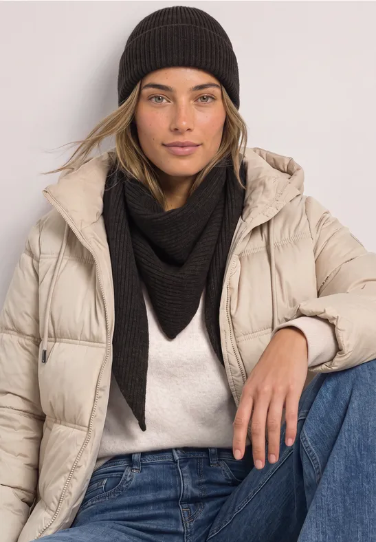 Jeune femme en doudoune beige, foulard triangulaire noir et bonnet devant un fond clair.