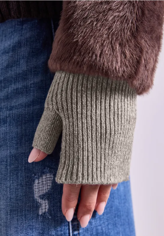 Gestrickter, fingerloser Handschuh an Hand, kombiniert mit flauschigem Mantelärmel und lässiger Jeans.