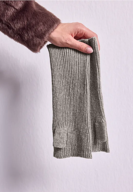 Eine Hand hält einen grauen, gerippten Strickschal vor hellgrauer Wand.