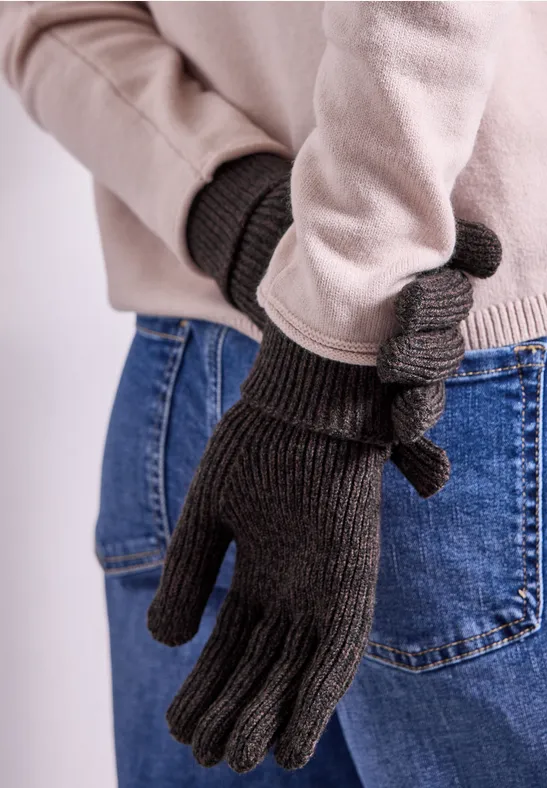 Braune Strickhandschuhe mit Knoten-Detail an einer Person in Jeans und beigem Pullover