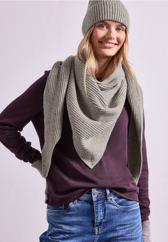 Frau in lila Pullover mit grauer Strickmütze und passendem Dreieckstuch lächelt in die Kamera.