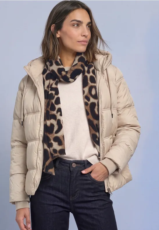 Femme en doudoune beige, pull crème, jean et écharpe léopard sur fond uni.