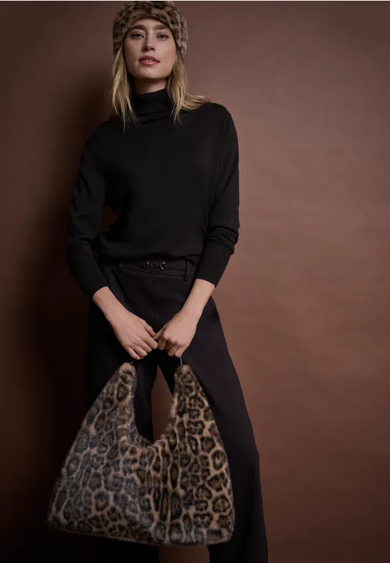 Frau in schwarzem Outfit mit Leo-Tuch und passender Leo-Tasche vor braunem Hintergrund.