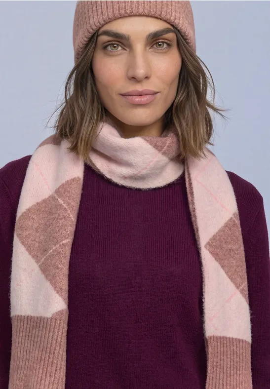 Frau mit rosa Beanie, rosa-weiß gemusterter Strickschal und dunkellila Pullover schaut ruhig in die Kamera.