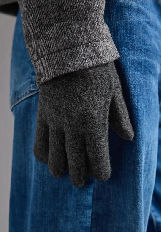 Een hand met een grijze wollen handschoen naast een blauwe spijkerbroek