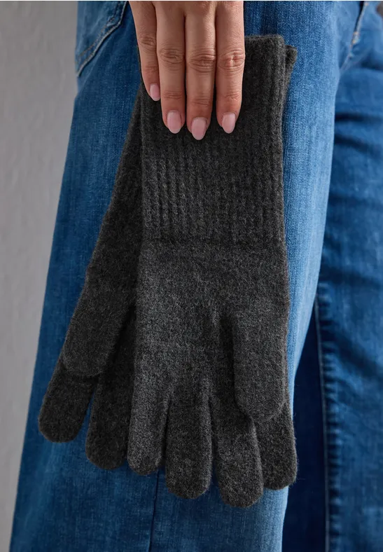 Een paar grijs gebreide winterhandschoenen bungelen aan iemands spijkerbroek.