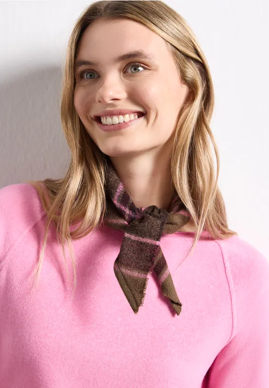 Eine lächelnde Frau mit langen blonden Haaren trägt einen pinken Pullover und ein braunes, gemustertes Halstuch.