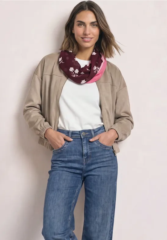 Een vrouw in een casual outfit met beige jasje, wit shirt, blauwe spijkerbroek en roze sjaal met print.