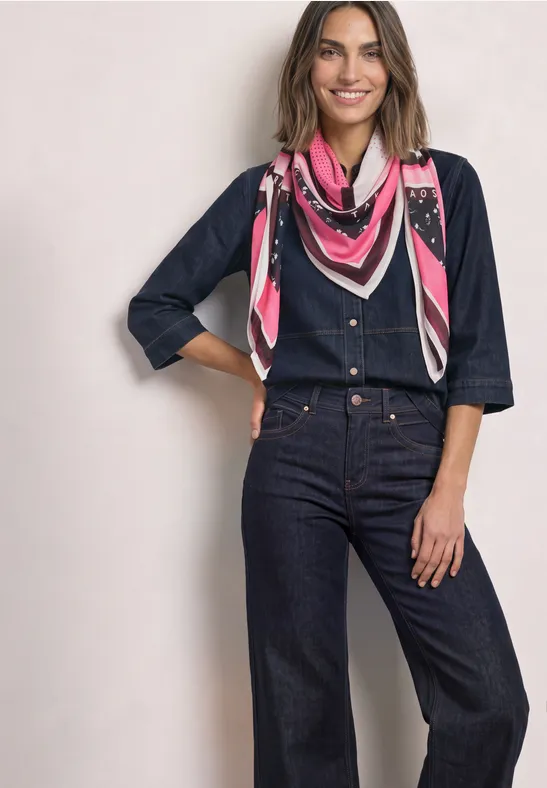 Frau in dunkelblauem Denim-Overall mit 3/4-Ärmeln und pinkem gemustertem Halstuch, lächelnd