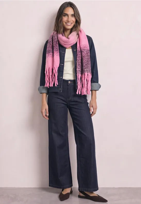 Frau in Jeansjacke, weißer Bluse, weiten Jeans, pinkem Schal und schwarzen Ballerinas vor hellem Hintergrund.