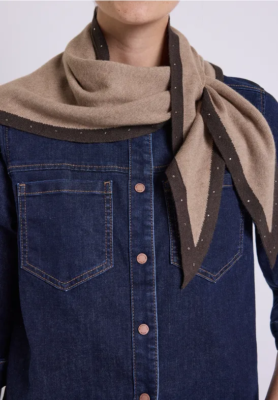 Veste en jean bleu foncé et écharpe beige ornée de perles, nouée sur le côté.