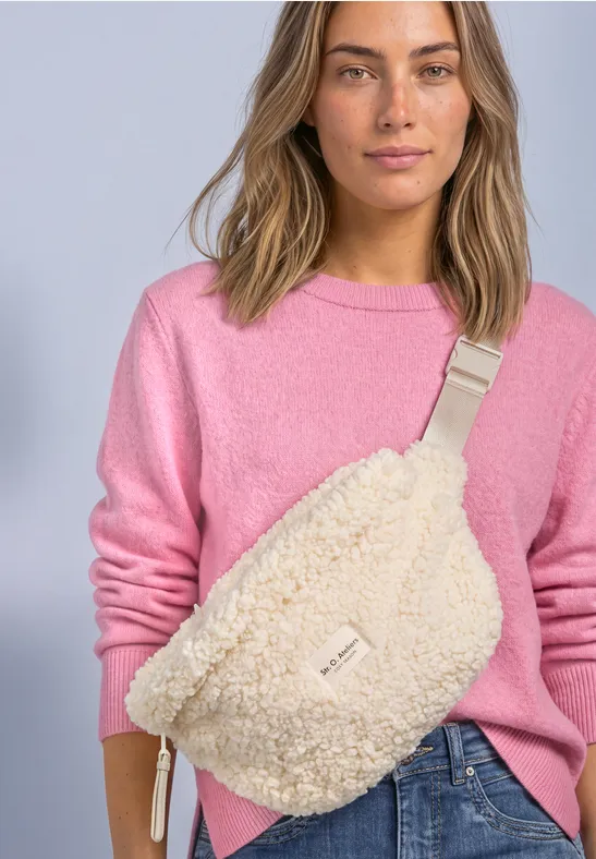 Frau in pinkem Pullover trägt gemütliche Teddy-Muster Gürteltasche über Jeans.