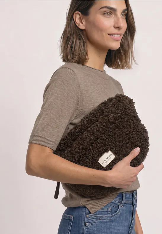 Frau in T-Shirt und Jeans hält flauschige braune Tasche vor dem Oberkörper.