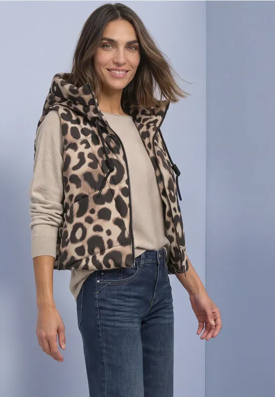 Frau trägt leichten, ärmellosen Weste mit Leopardenmuster über einem beigen Pullover und Jeans und lächelt.