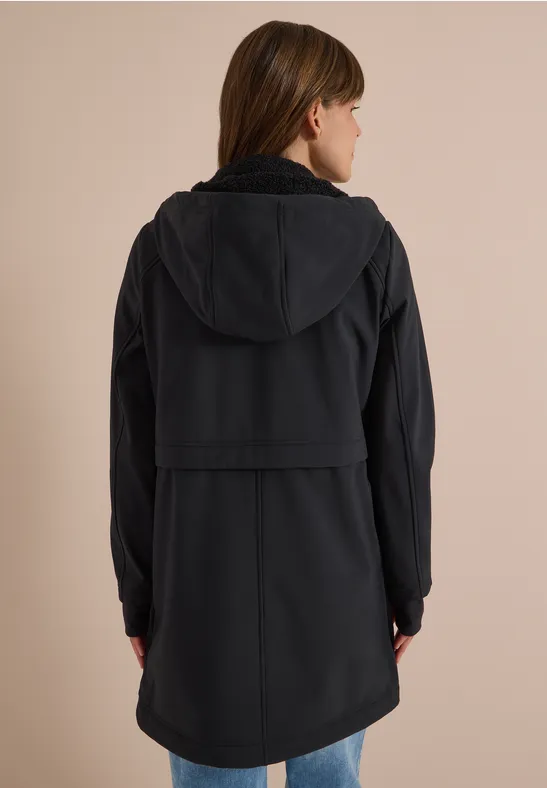 Personne en manteau noir à capuche, vue de dos sur fond neutre.