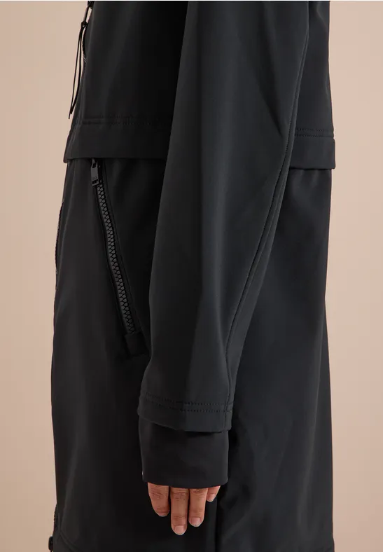 Détail latéral d'une veste noire portée, avec poches zippées et manches longues.