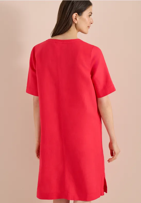 Eine Frau trägt ein schlichtes rotes Kleid, Rückenansicht.