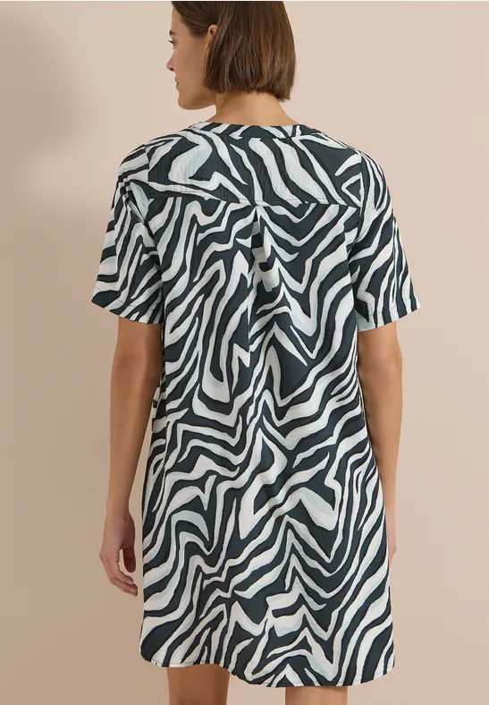 Frau in kurzem, zebra-gestreiftem Kleid, Rückenansicht vor neutralem Hintergrund.