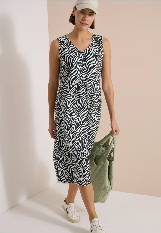 Frau in Zebra-Midikleid, weißer Sneaker, grüne Handtasche – lässiger, moderner Look.