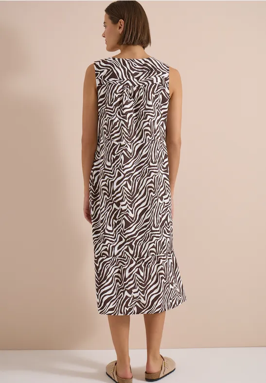 Frau in ärmellosem Midi-Kleid mit Zebramuster, Rückansicht, trägt flache Sandalen.