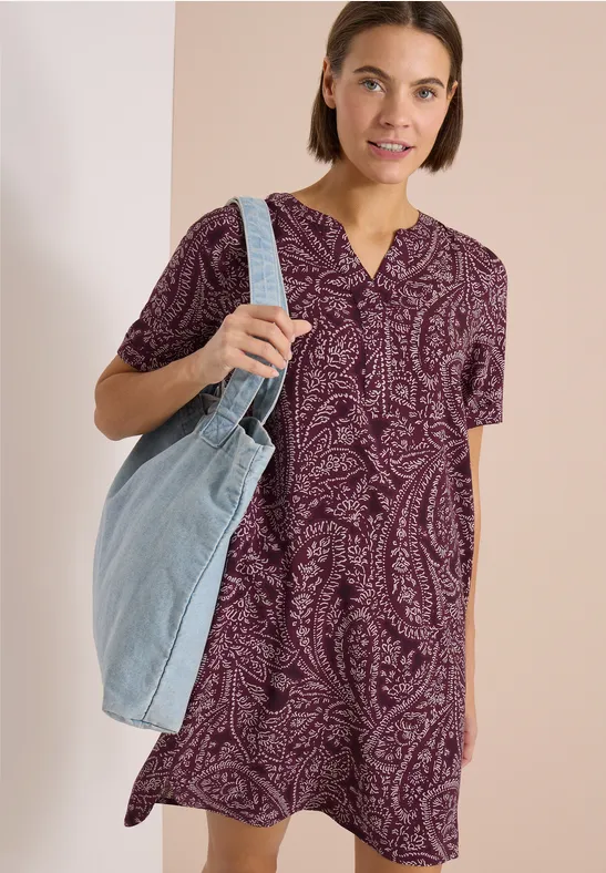 Frau in lila Paisley-Kleid mit V-Ausschnitt trägt große hellblaue Jeans-Umhängetasche.