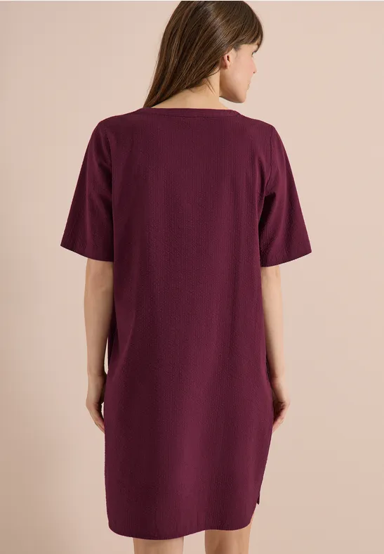 Frau in lockerem lila Kleid, Rückenansicht.