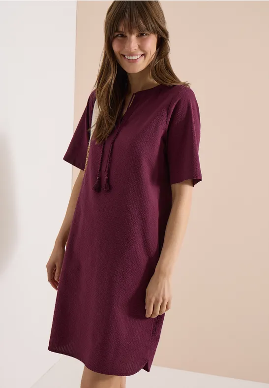 Frau trägt legeres, bordeauxfarbenes T-Shirt-Kleid mit Kapuze und kurzen Ärmeln.