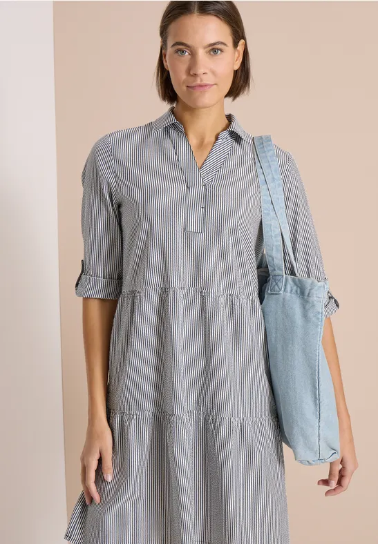 Frau in hellgrauem, knielangem Hemdkleid mit 3/4-Ärmeln und Jeans-Schultertasche.