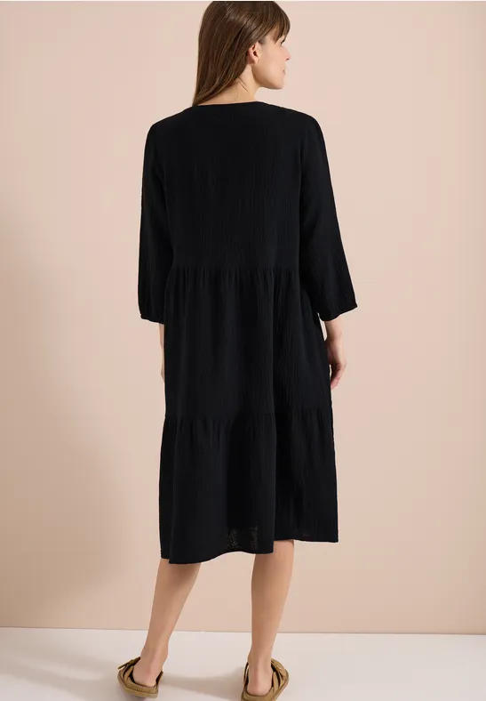 Femme vue de dos portant une robe midi noire à volants et manches 3/4.